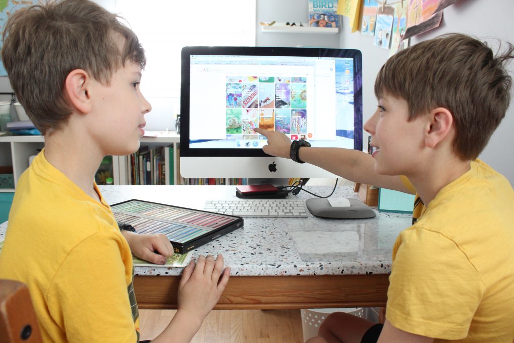Boys point at computer screen with art lesson calendar shown